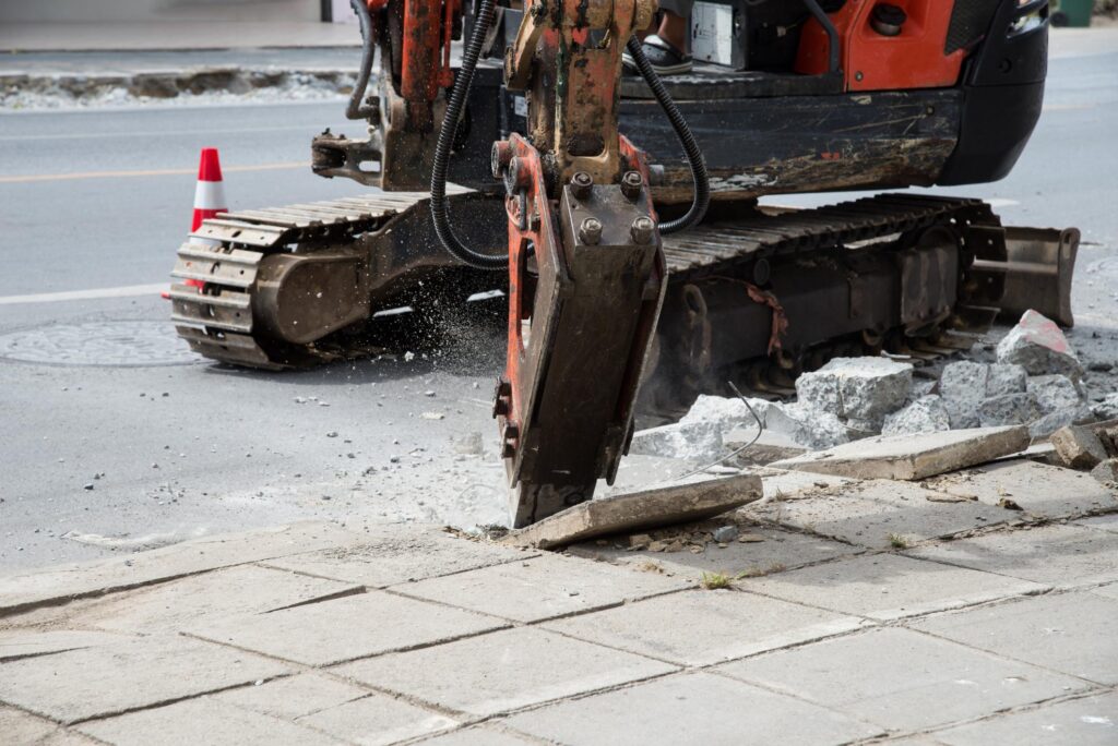 "a bulldozer digging through a street next to a sidewalk"
