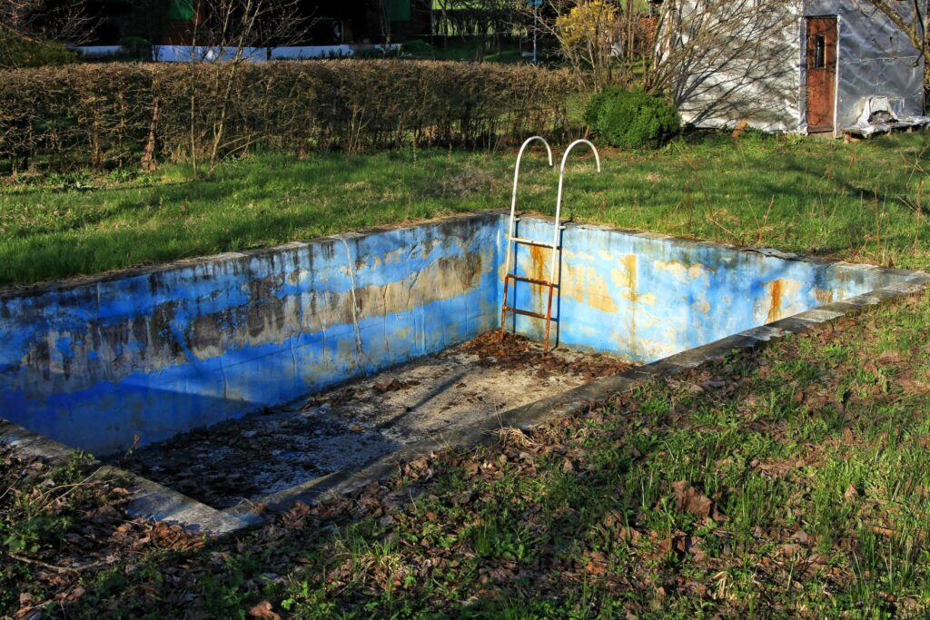 "an old abandoned swimming pool in a field"
